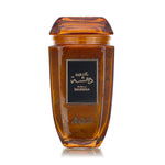 A glass jar with a brown liquid inside, presumably the Dahsha Bakhoor, with a black label on the front and a wooden lid on top.