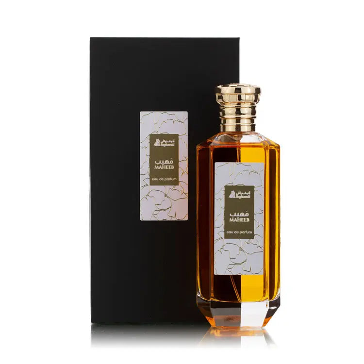 Maheeb eau de parfum bottle with golden cap standing beside a black box with a floral patterned label in olive green and gold