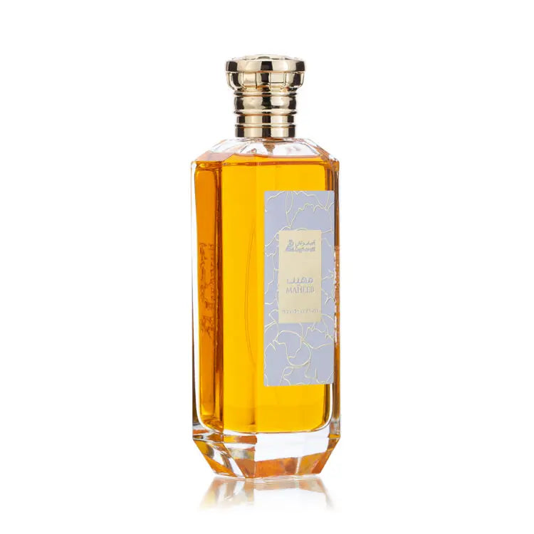 A clear hexagonal glass perfume bottle with a golden cap, filled with amber-colored liquid and labeled 'Maheeb eau de parfum' with a light purple and gold design